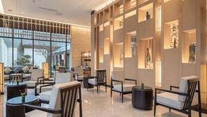 En moderne hotellobby med siddeområder, store vinduer og dekorative vægpaneler.