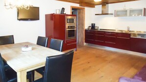 Un coin repas avec une table et des chaises, une cuisine rouge dotée d’un four à micro-ondes et d’un four traditionnel, et un fauteuil violet.