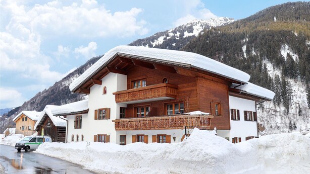 Un chalet en bois doté d’un balcon, entouré de montagnes enneigées.