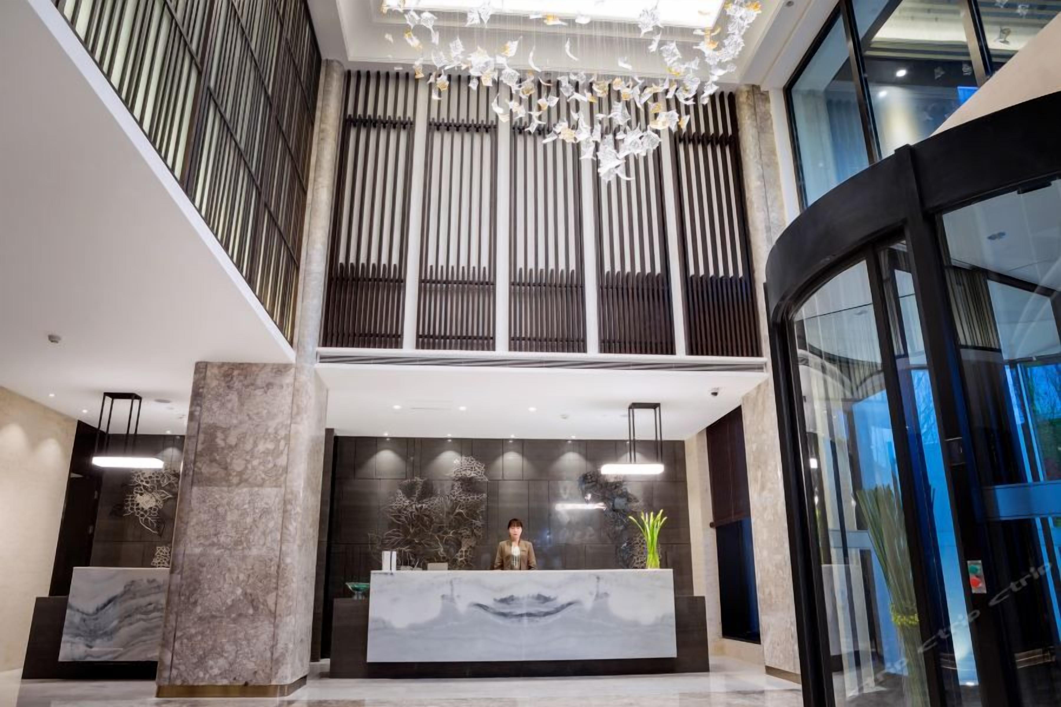 A modern reception area with a marble reception desk, vertical blinds, and a chandelier.