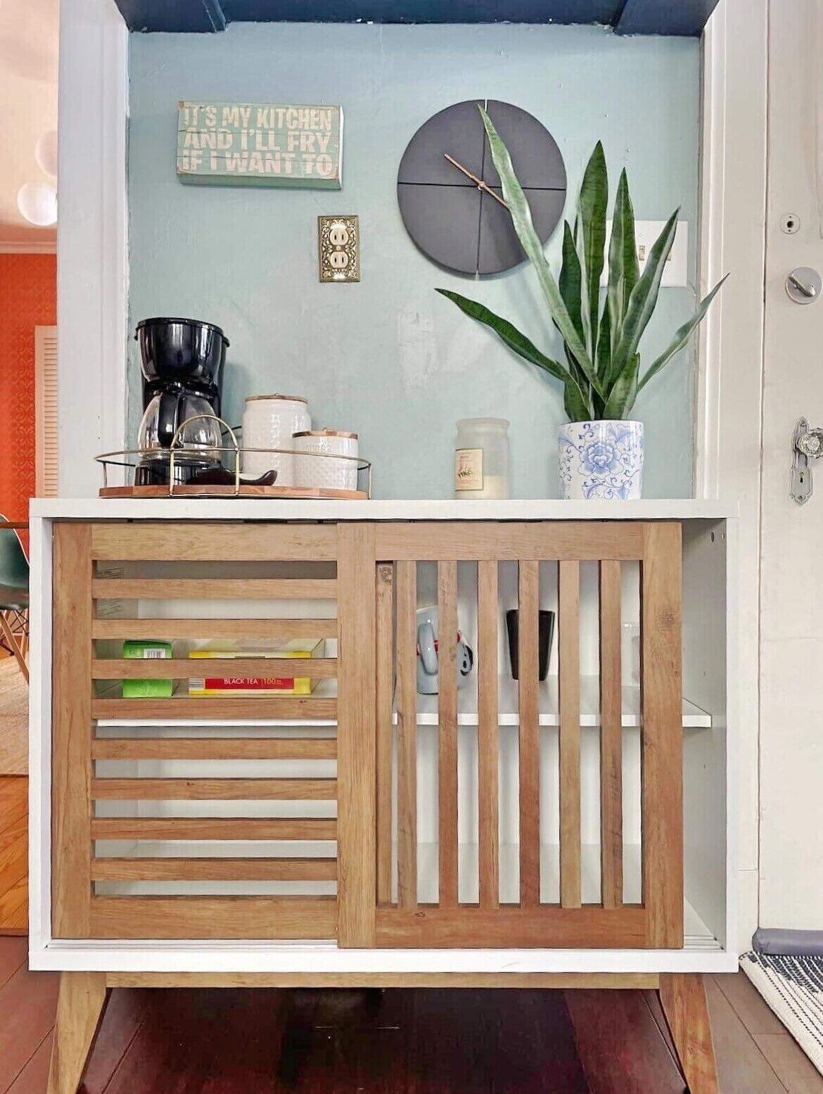 A kitchen area with a coffee maker, a potted plant, and a sign on the wall.