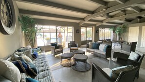 Ein großzügiger Wohnbereich mit einer breiten Couch, mehreren Sesseln und einem Couchtisch. Große Fenster sorgen für natürliches Licht und Blick ins Freie.