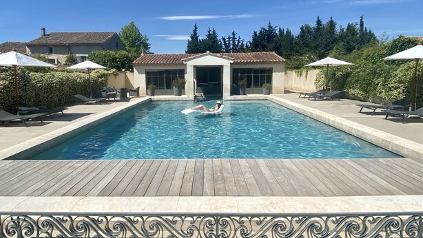 Ein rechteckiger Swimmingpool mit Holzterrasse im Vordergrund, umgeben von Liegestühlen und Sonnenschirmen.