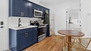 Une cuisine moderne avec des meubles de couleur bleu foncé, des appareils en acier inoxydable et une table ronde en bois, accompagnée de deux chaises en osier.