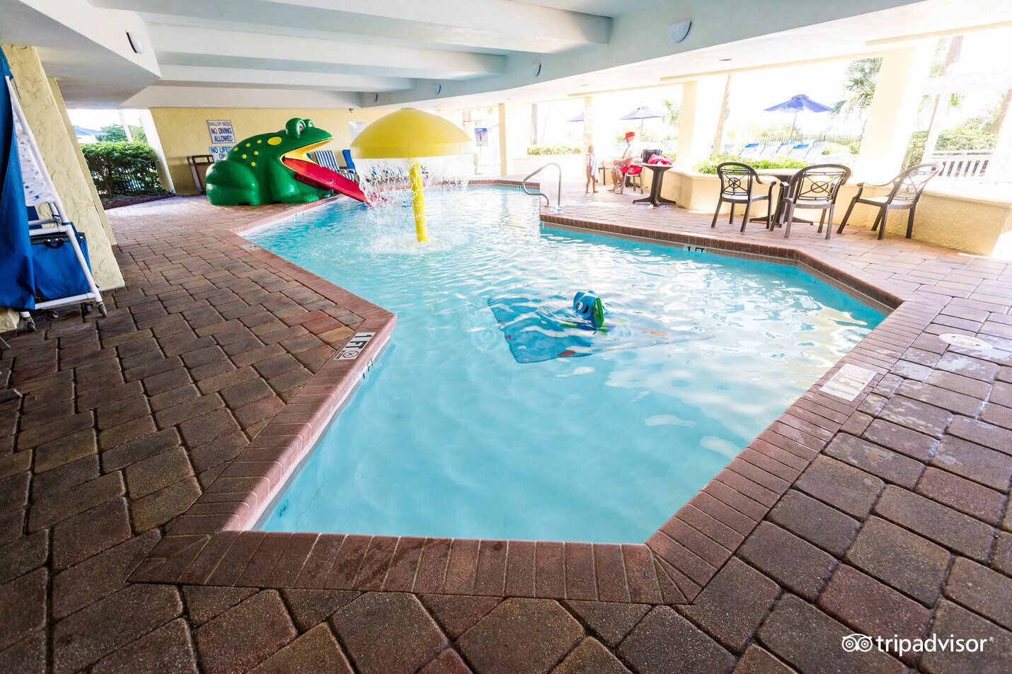An indoor pool with a water slide, lounge chairs, and a covered patio area.