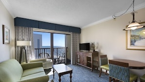 A hotel room with a balcony, a dining area, a TV, and a painting on the wall.