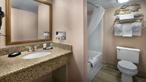 Une salle de bain avec un lavabo surmonté d’un plan de travail en granit, un grand miroir, un rideau de douche et des toilettes.