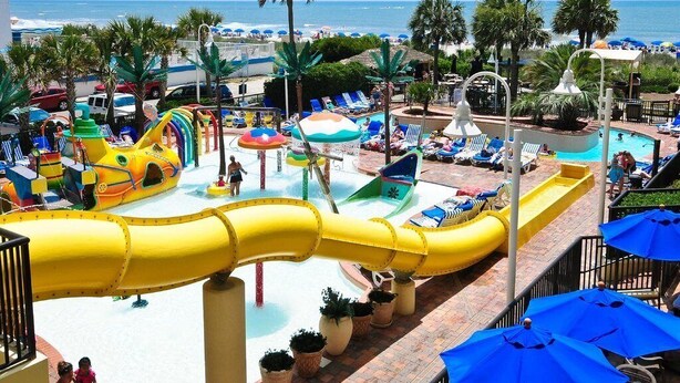 Un parc aquatique avec des toboggans et des piscines, des palmiers et une vue sur la plage.