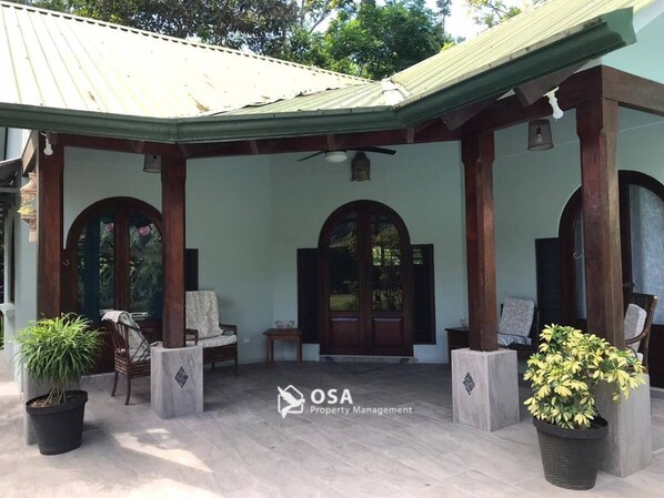 A covered outdoor seating area with two wooden chairs, a small table, and potted plants.