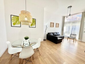 A modern living room with a glass dining table, black sofa, and a large window with a view. - Aluche Aparment B (Madrid)