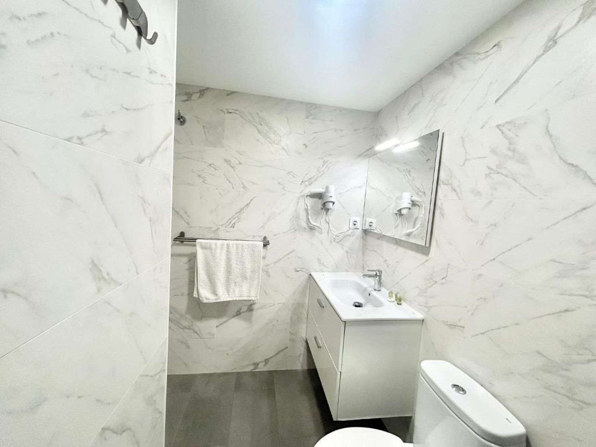 Un baño con pared de mármol, un lavabo, un inodoro y un perchero para toallas.
