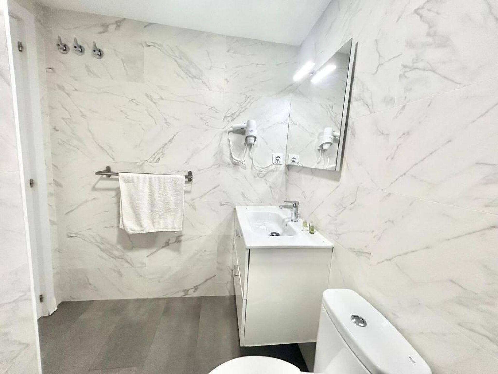 A bathroom with a white sink, mirror, and toilet, marble walls, and a towel hanging on a rack.