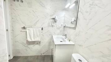 A bathroom with a white sink, mirror, and toilet, marble walls, and a towel hanging on a rack.