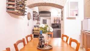 A dining area with a wooden table and chairs, a wine rack on the wall, and a kitchen in the background. - The wine cave _Stylish 110sqm Flat, Strong WiFi, AC, Milan Central Station (Milano)