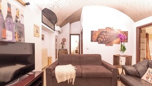 A living room with a brown sofa, a flat-screen TV, and wall art including wine bottles and a vineyard scene. - The wine cave _Stylish 110sqm Flat, Strong WiFi, AC, Milan Central Station (Milano)