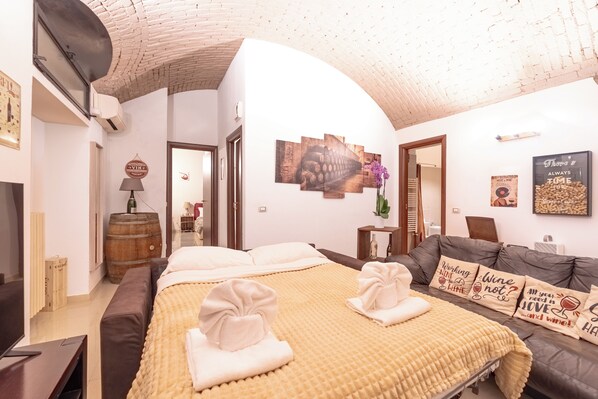 Habitación de hotel con cama, sofá y mesa de comedor. En la pared, un reloj y un cuadro.