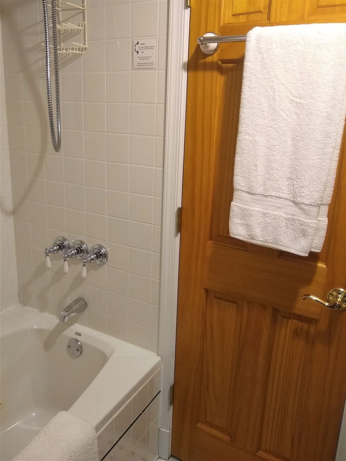A bathroom with a bathtub, a shower, and a wooden door with a towel hanging on it.