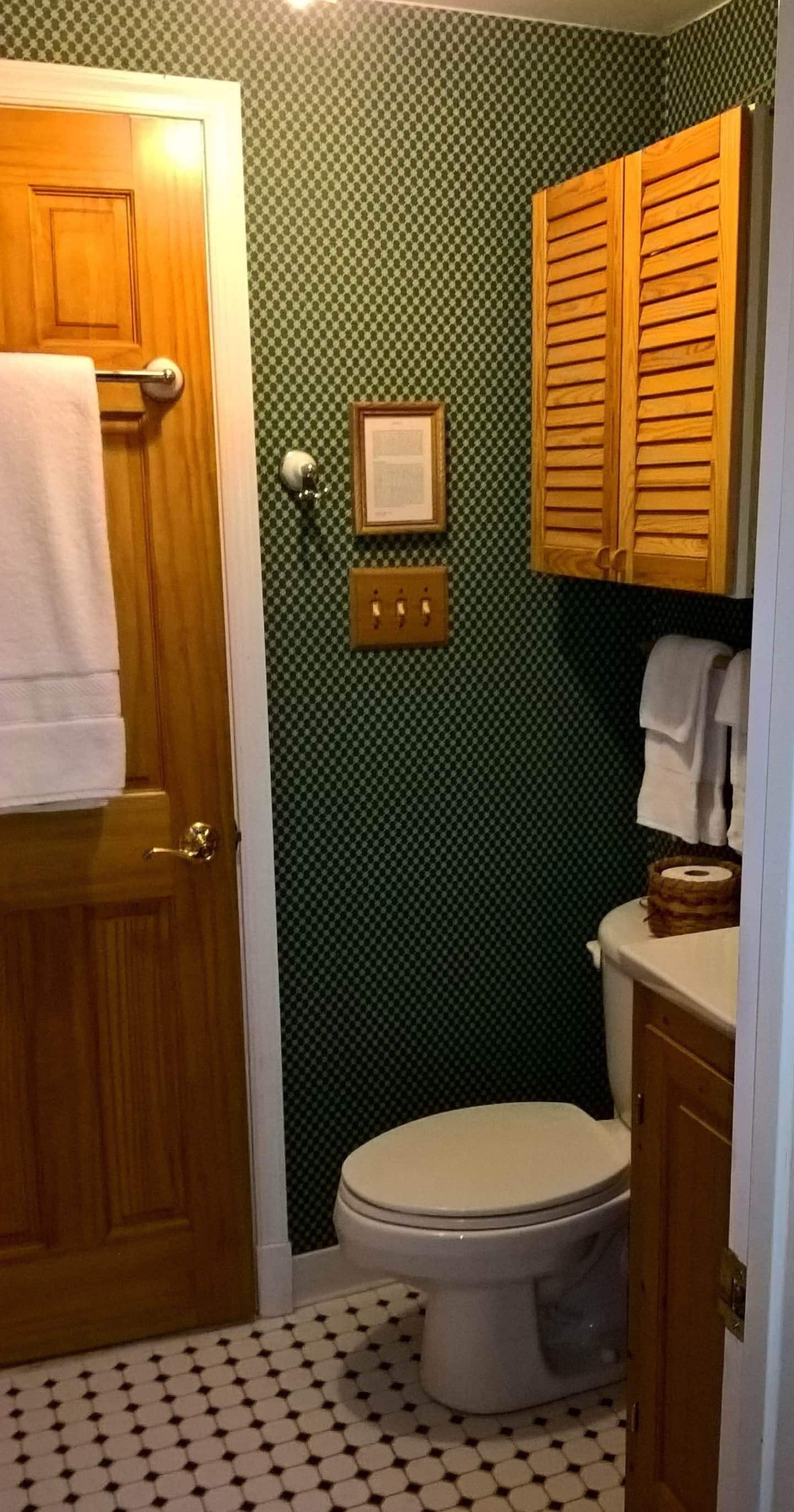 Ein Badezimmer mit Holztür, Toilette, Waschbecken mit Holzschrank und einem Musterboden.