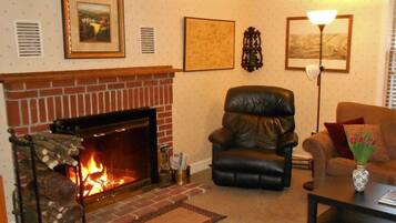 A living room with a brick fireplace, a leather armchair, a sofa, a coffee table, and wall-mounted artwork.