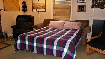 A bedroom with a bed, a chair, a desk, a lamp, and a window with blinds.