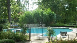 A swimming pool surrounded by a fence, with a bench and a small tree in the foreground. - Rollingside Guest Suite (Catonsville)