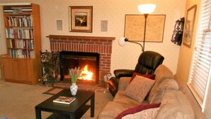 A living room with a fireplace, a leather armchair, a bookshelf, and a coffee table with a vase of flowers. - Rollingside Guest Suite (Catonsville)