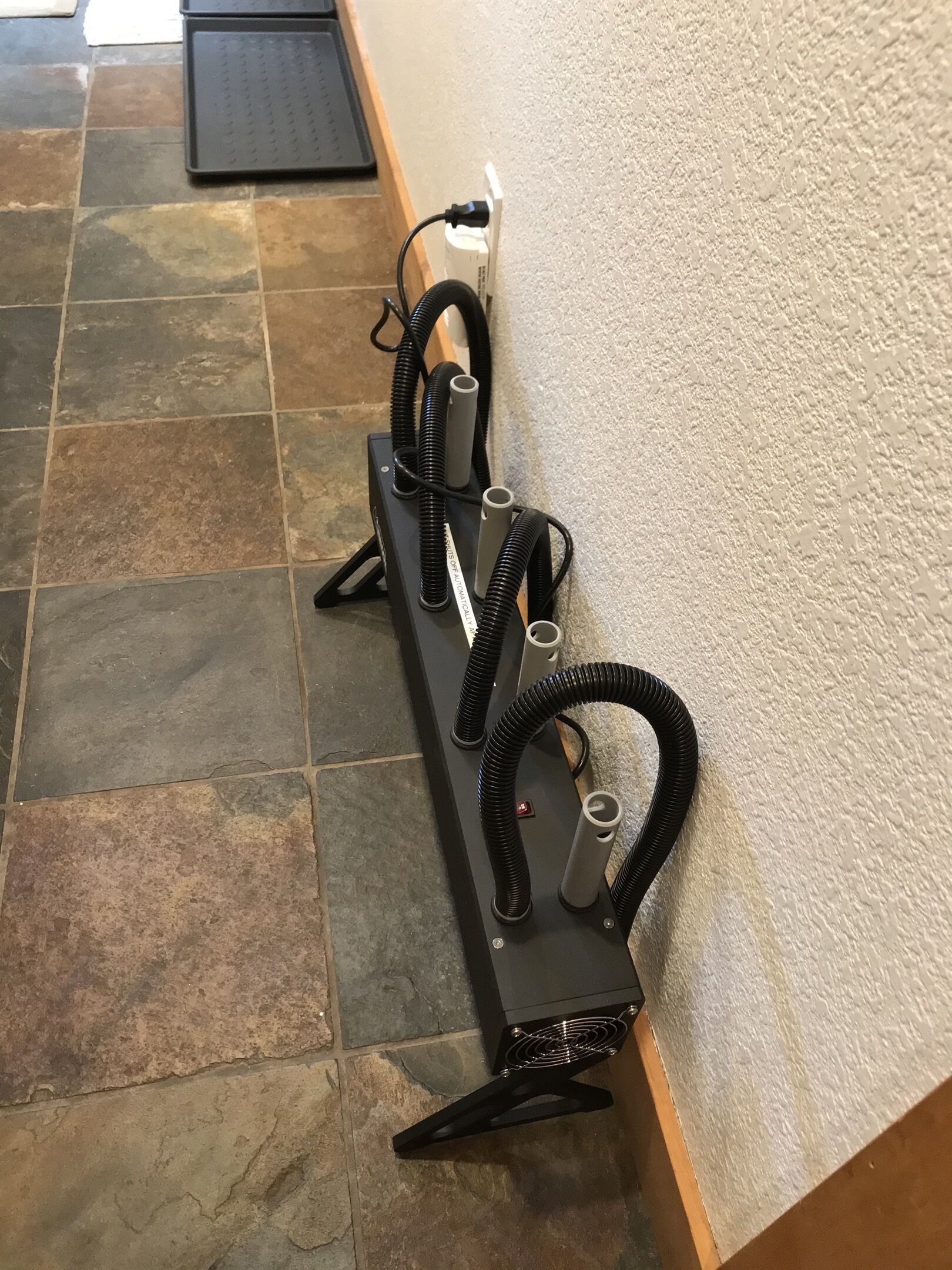 A black portable heater with coiled hoses and a power cord plugged into a wall socket.