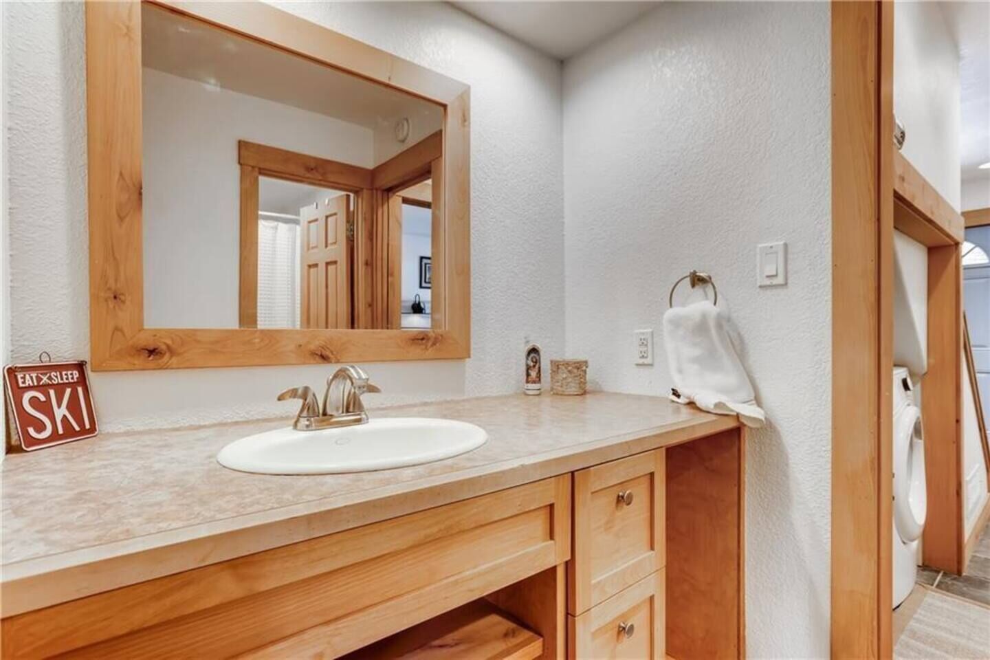 Een badkamer met een houten wastafelmeubel, een witte wasbak en een spiegel.