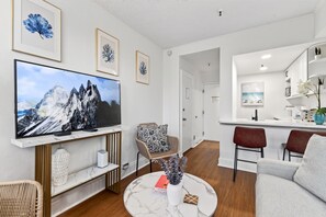 A modern living room with a flat-screen TV, a round coffee table, and a dining area with a bar.