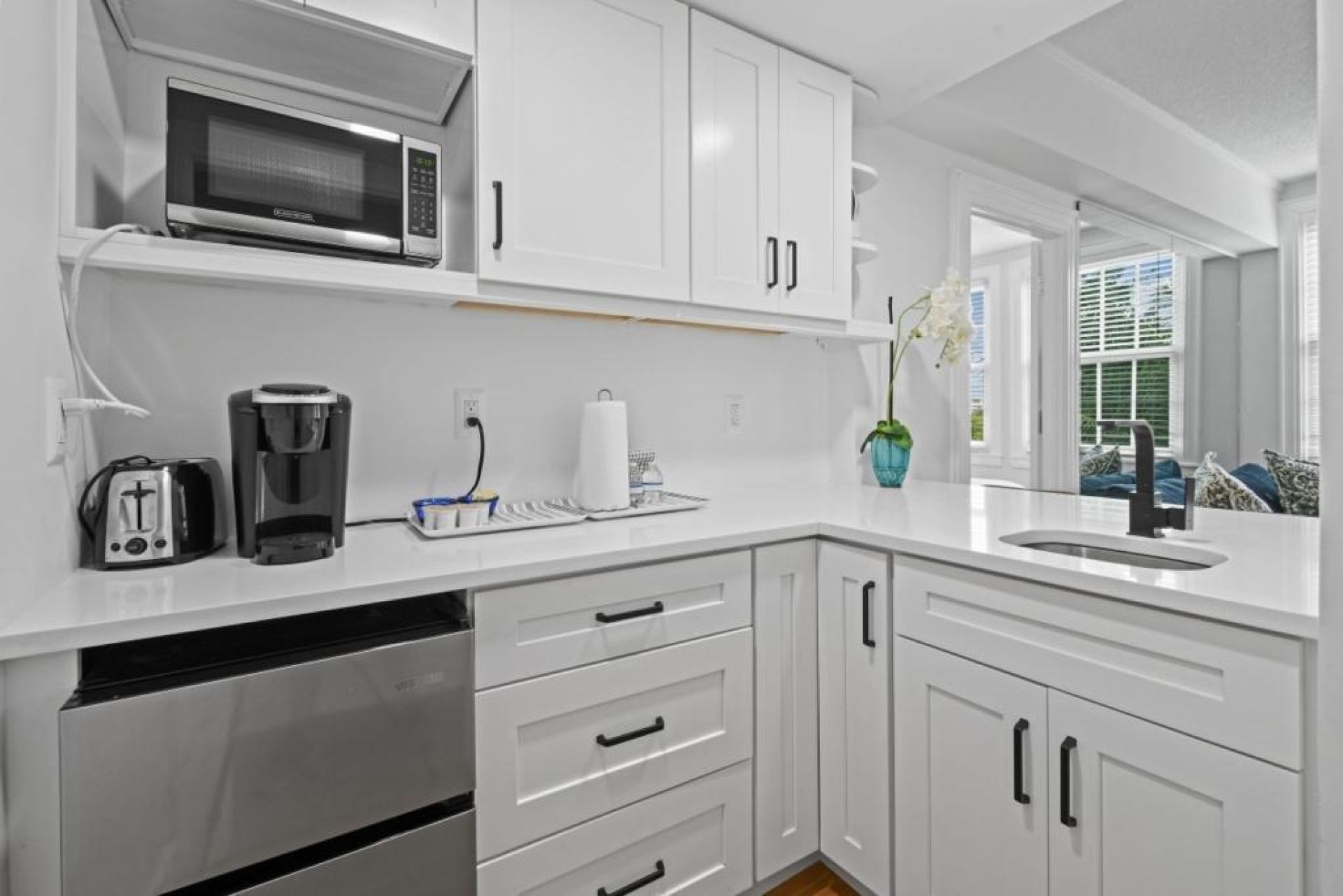 Una cocina moderna con armarios blancos, microondas integrado, cafetera y lavaplatos.