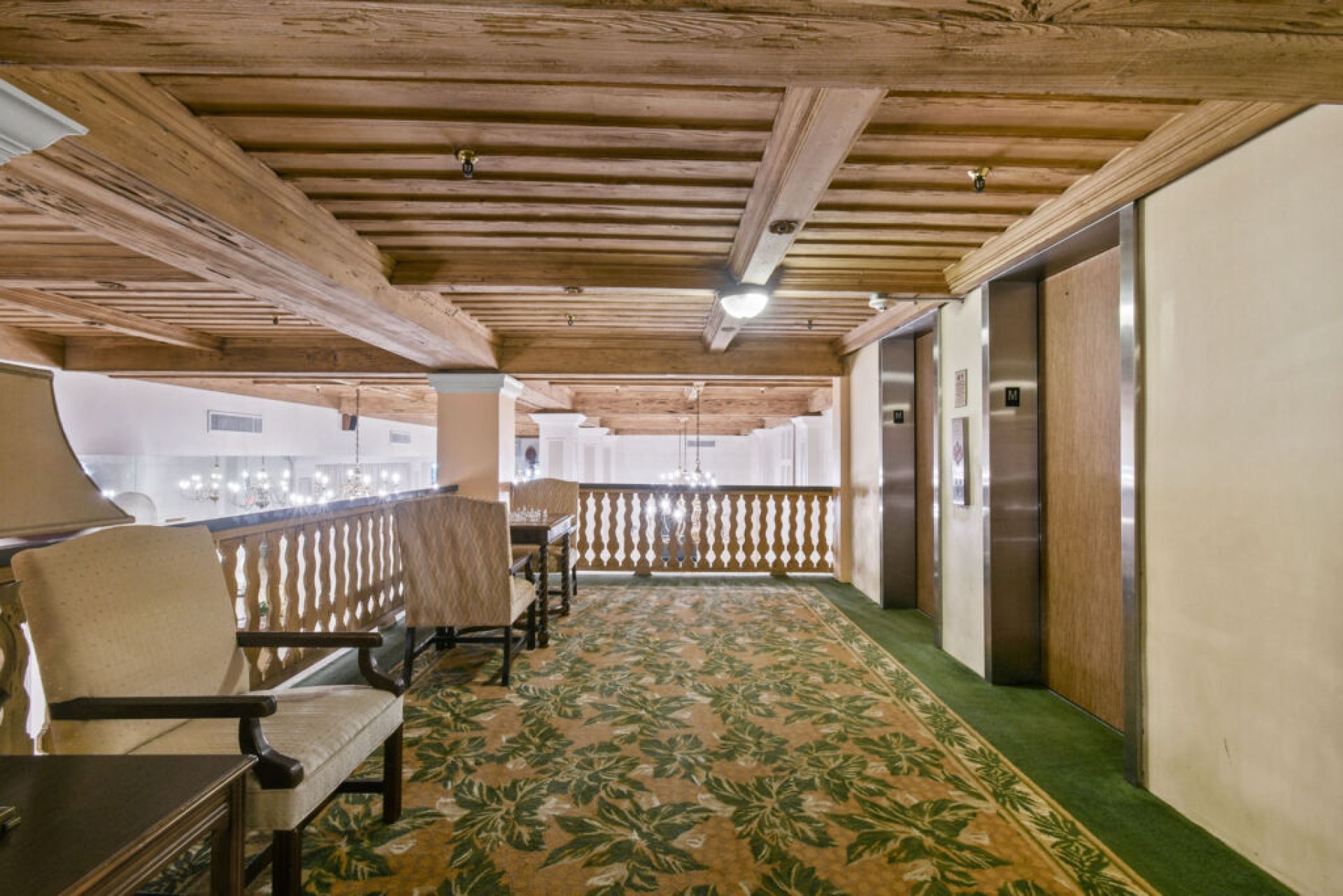 A corridor with wooden beams, a patterned carpet, and a seating area with chairs.