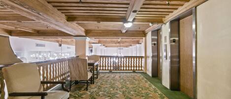 A corridor with wooden beams, a patterned carpet, and a seating area with chairs.
