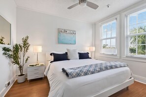 A bedroom with a bed, two bedside tables, a floor lamp, a ceiling fan, a window with blinds, and a wall-mounted painting. - Condo/Pool/StepsToBeachDine/Island 1br (Palm Beach)
