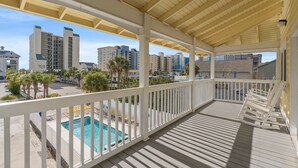 A covered outdoor area with a pool, white railings, and a view of high-rise buildings. - Ruby Waves- Beach House with Private Pool, Short Walk to the Beach (North Myrtle Beach)