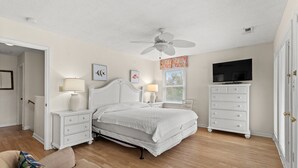 A bedroom with a bed, nightstands, a dresser, a television, and a ceiling fan. - Ruby Waves- Beach House with Private Pool, Short Walk to the Beach (North Myrtle Beach)