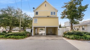 A two-story yellow house with a garage entrance, surrounded by greenery and a clear sky. - Ruby Waves- Beach House with Private Pool, Short Walk to the Beach (North Myrtle Beach)