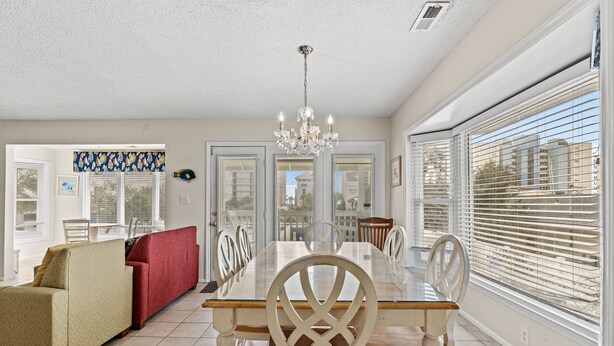 A spacious dining area with a glass table and white chairs, a red sofa, and a chandelier. - Ruby Waves- Beach House with Private Pool, Short Walk to the Beach (North Myrtle Beach)