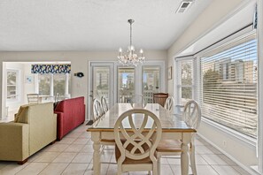 A spacious dining area with a glass table and white chairs, a red sofa, and a chandelier.