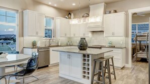 Una cocina moderna con armarios blancos, una isla central con almacenamiento para vinos y vistas a un edificio tradicional.