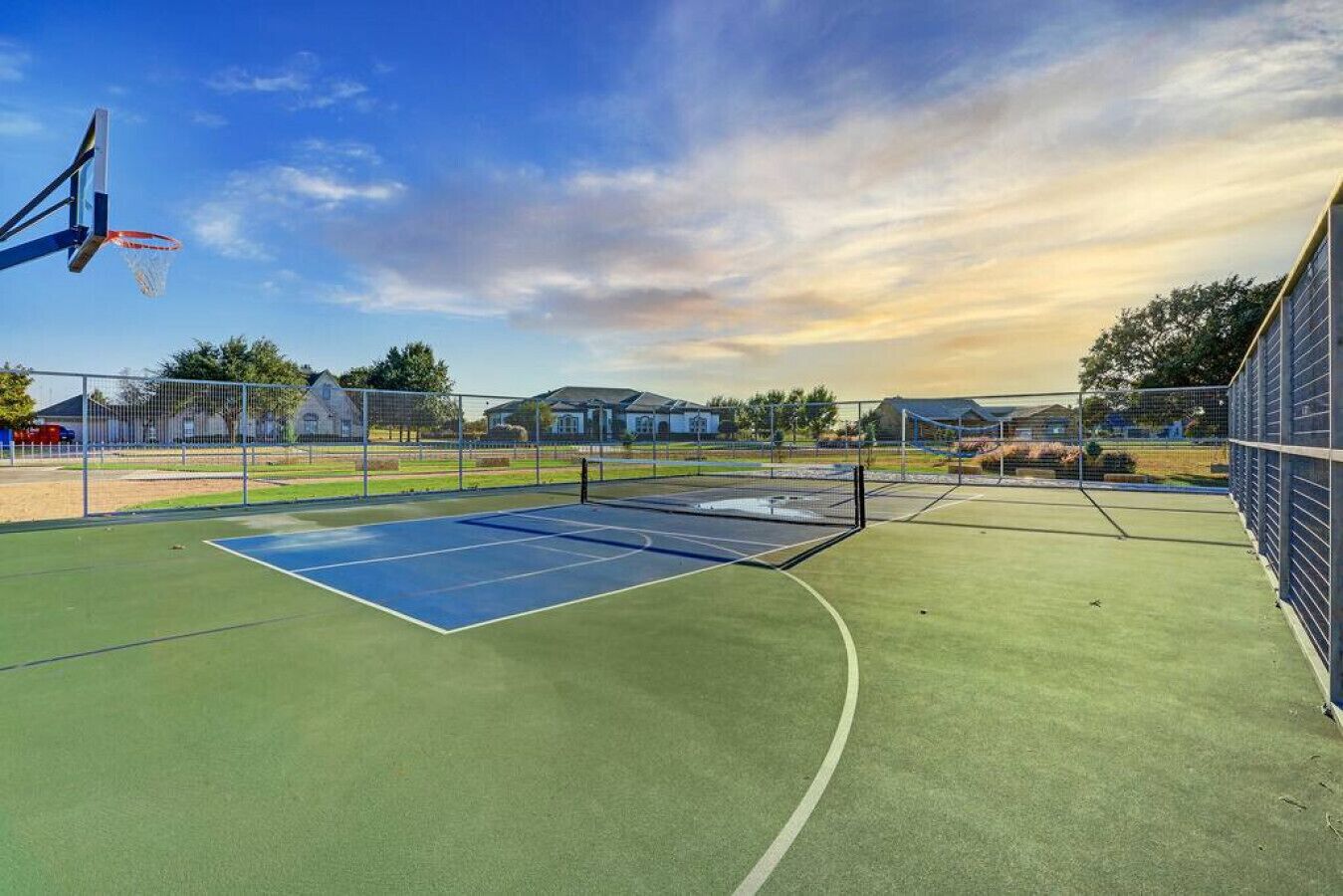 An outdoor basketball court with a blue playing surface and a net.