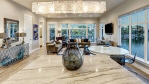 Un salón amplio con una gran mesa redonda, un jarrón decorativo y vista a un cuerpo de agua a través de amplias ventanas.