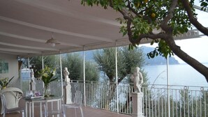 A covered terrace with a table and chairs, a vase of flowers, and a view of the sea and mountains. - Little Ludovica - Panoramic terrace by the sea (Ravello)