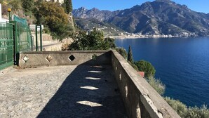 A stone pathway leading to a scenic overlook with a view of a body of water and mountains. - Little Ludovica - Panoramic terrace by the sea (Ravello)