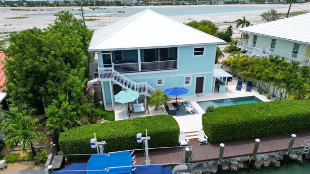 A two-story house with a balcony, a swimming pool, and a dock with a covered boat. - Paradise Found ~ Waterfront Pool Home, 50' Dock, Kayaks & Bikes (Marathon)