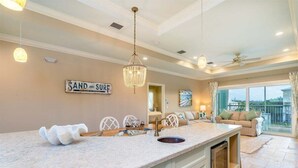 A kitchen with a large island, a chandelier, and a sign that reads "SAND AND SURF". - Paradise Found ~ Waterfront Pool Home, 50' Dock, Kayaks & Bikes (Marathon)