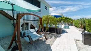 A patio with a swing chair, a pool, and a covered seating area. - Paradise Found ~ Waterfront Pool Home, 50' Dock, Kayaks & Bikes (Marathon)