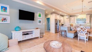 A modern living room with a flat-screen TV, a white entertainment unit, and a round coffee table with a starfish decoration. - Paradise Found ~ Waterfront Pool Home, 50' Dock, Kayaks & Bikes (Marathon)