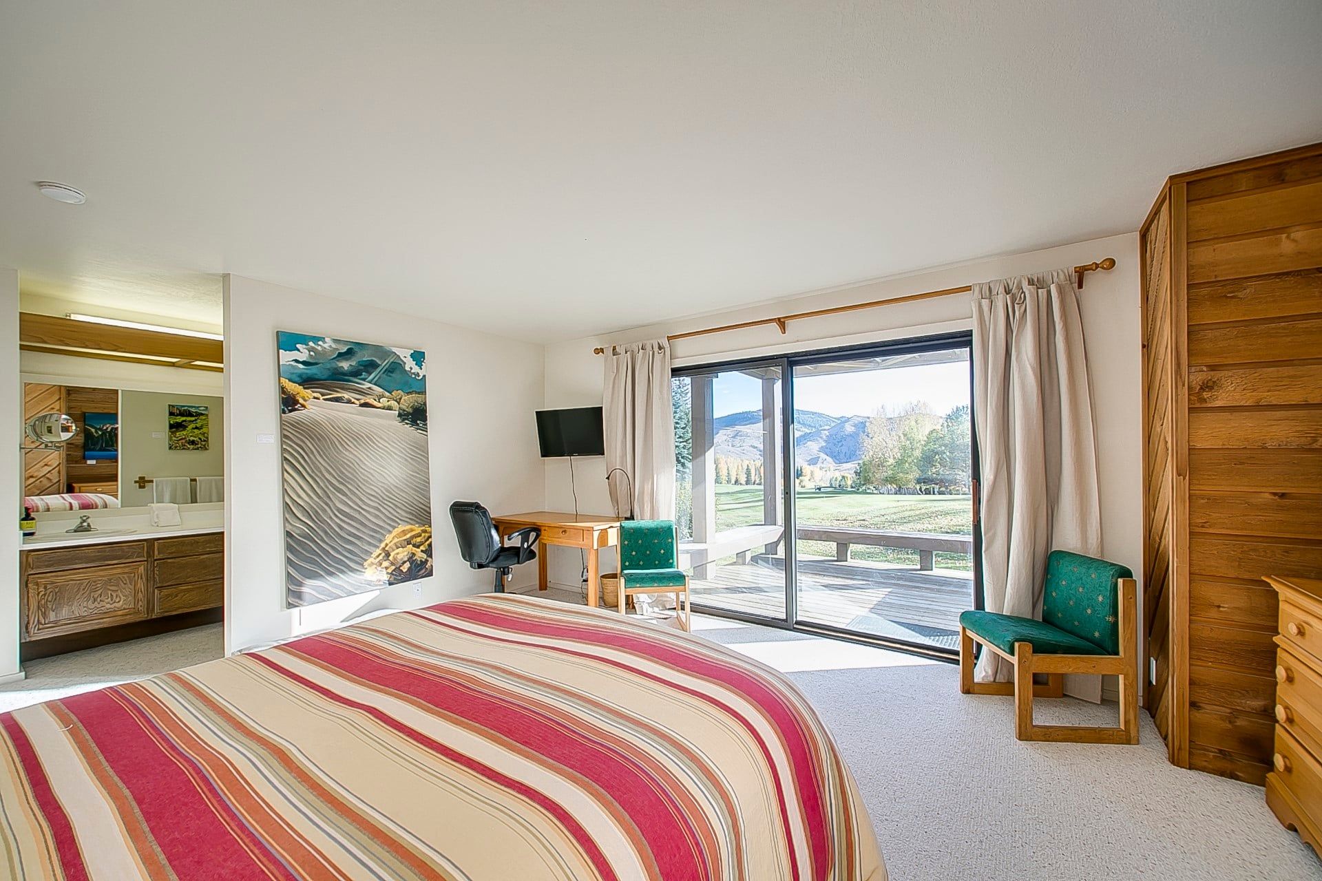 Habitación de hotel con una cama grande, un escritorio, una silla, un televisor y una puerta corrediza de vidrio que da a un espacio al aire libre.