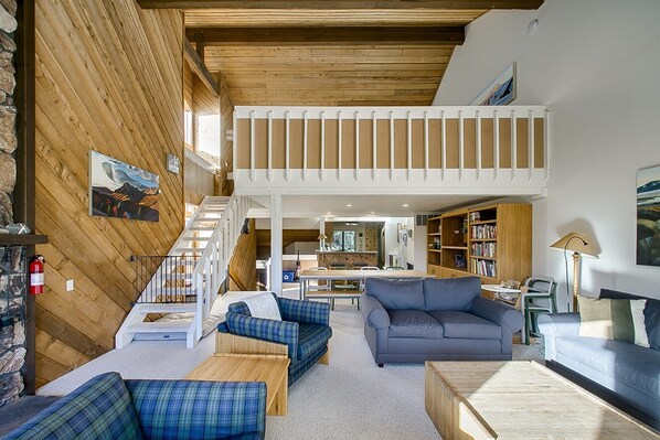 A spacious loft-style living area with a high ceiling, wooden beams, and a mezzanine level.