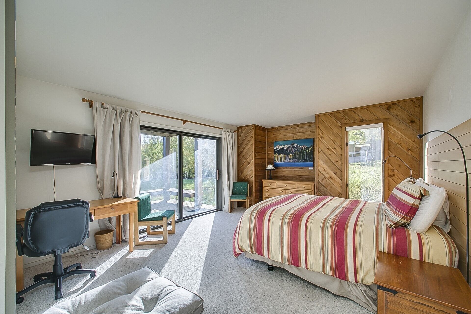 A bedroom with a bed, a desk, a chair, a TV, and a painting on the wall.